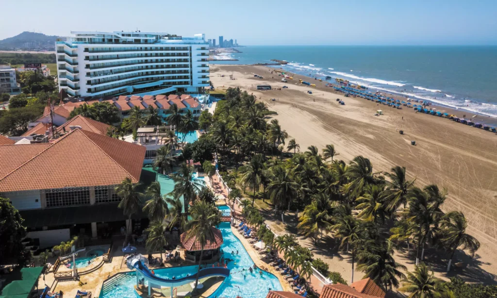 Vista aérea de un resort con piscinas, palmeras y una playa con sombrillas y el mar Caribe.
