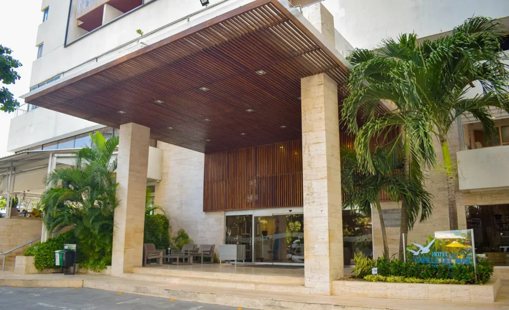 Entrada principal del Hotel Capilla del Mar con columnas de mármol, techo de madera y palmeras.